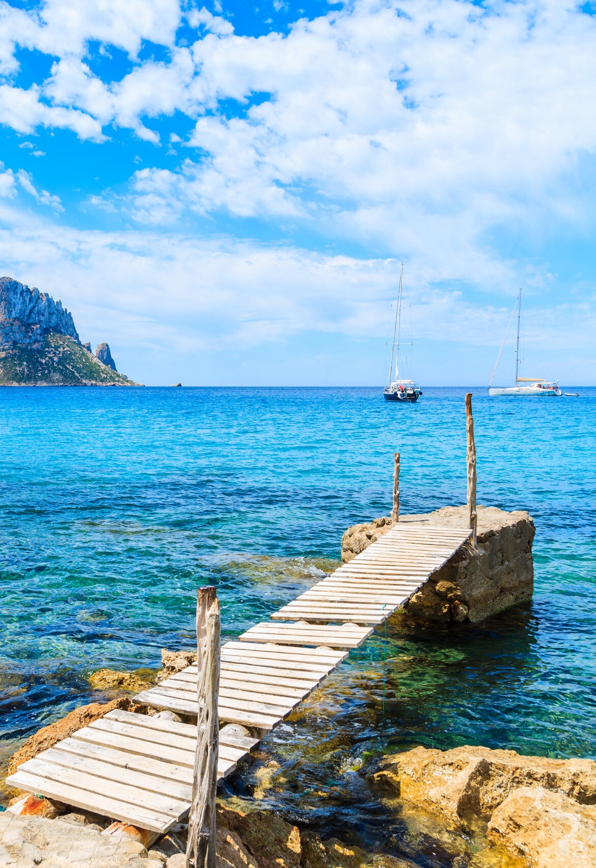 Small wooden pier in Cala d'Hort bay and view of Es Vedra island, Ibiza island, Spain